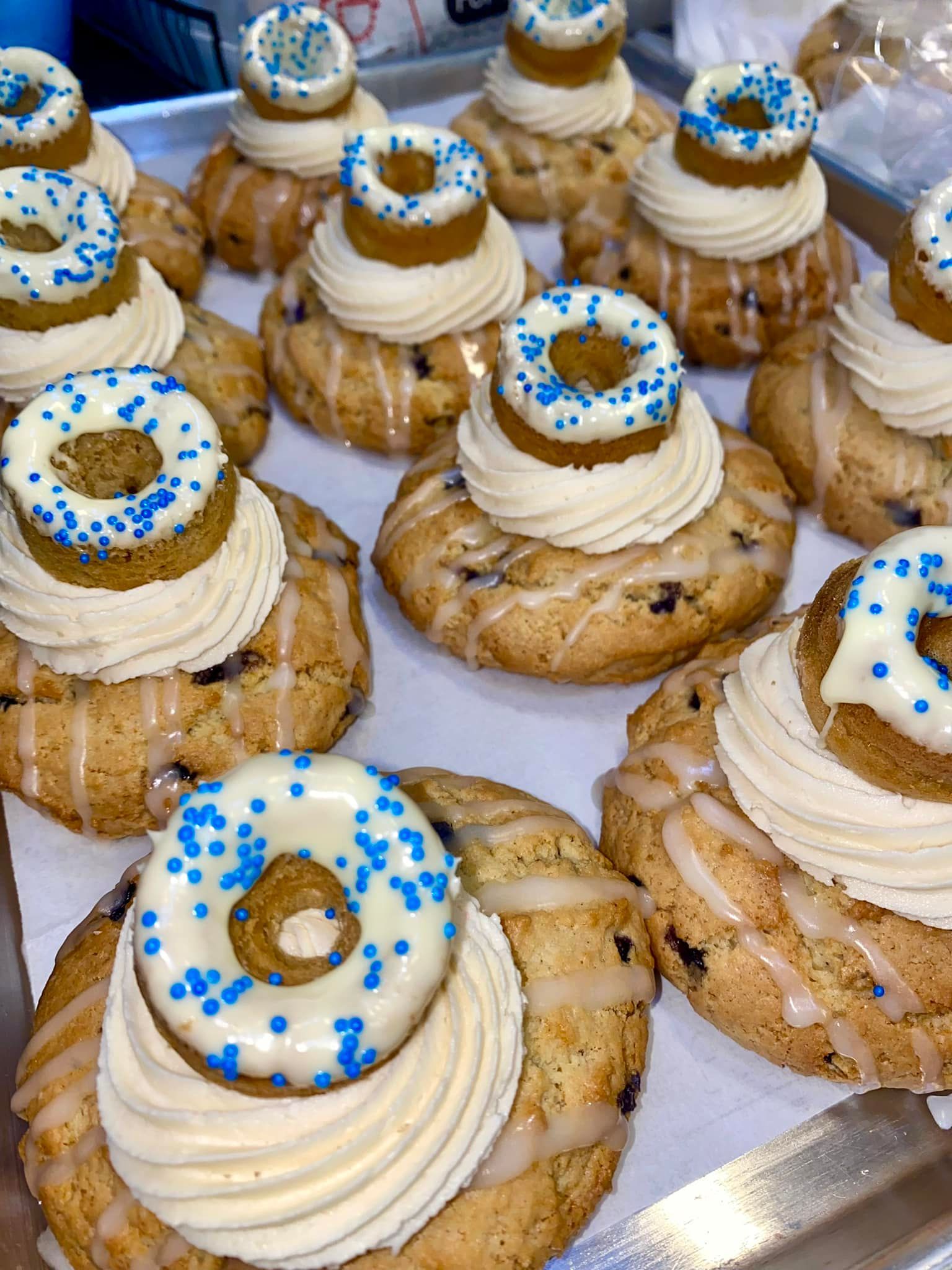 Tray of blueberry scones topped with buttercream, glaze, and mini donuts with blue sprinkles.