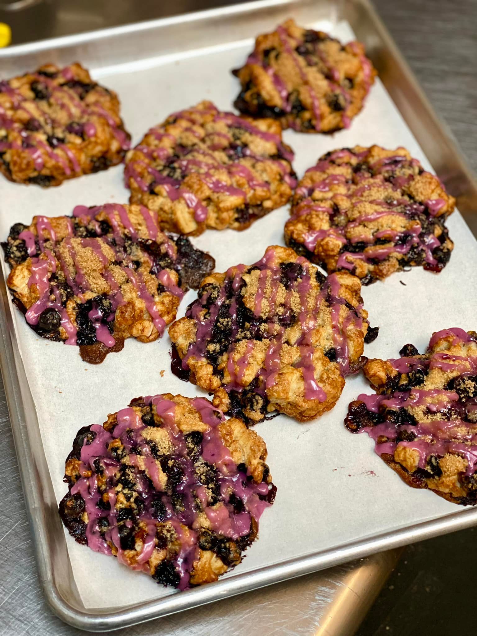 Baked scones with blueberries and pink glaze on a baking sheet.