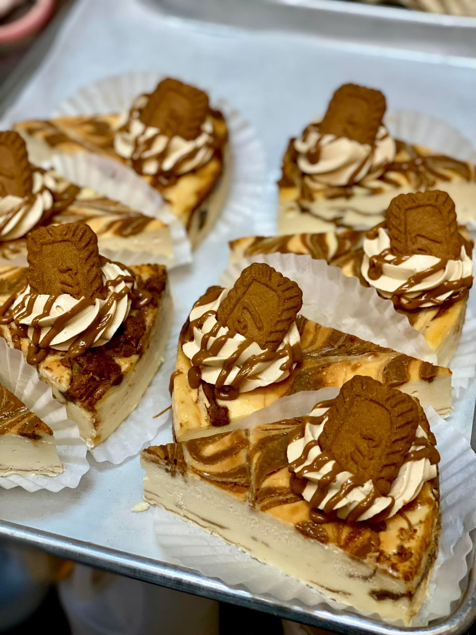 Slices of cheesecake swirled with caramel and topped with whipped cream and a cookie on a tray.