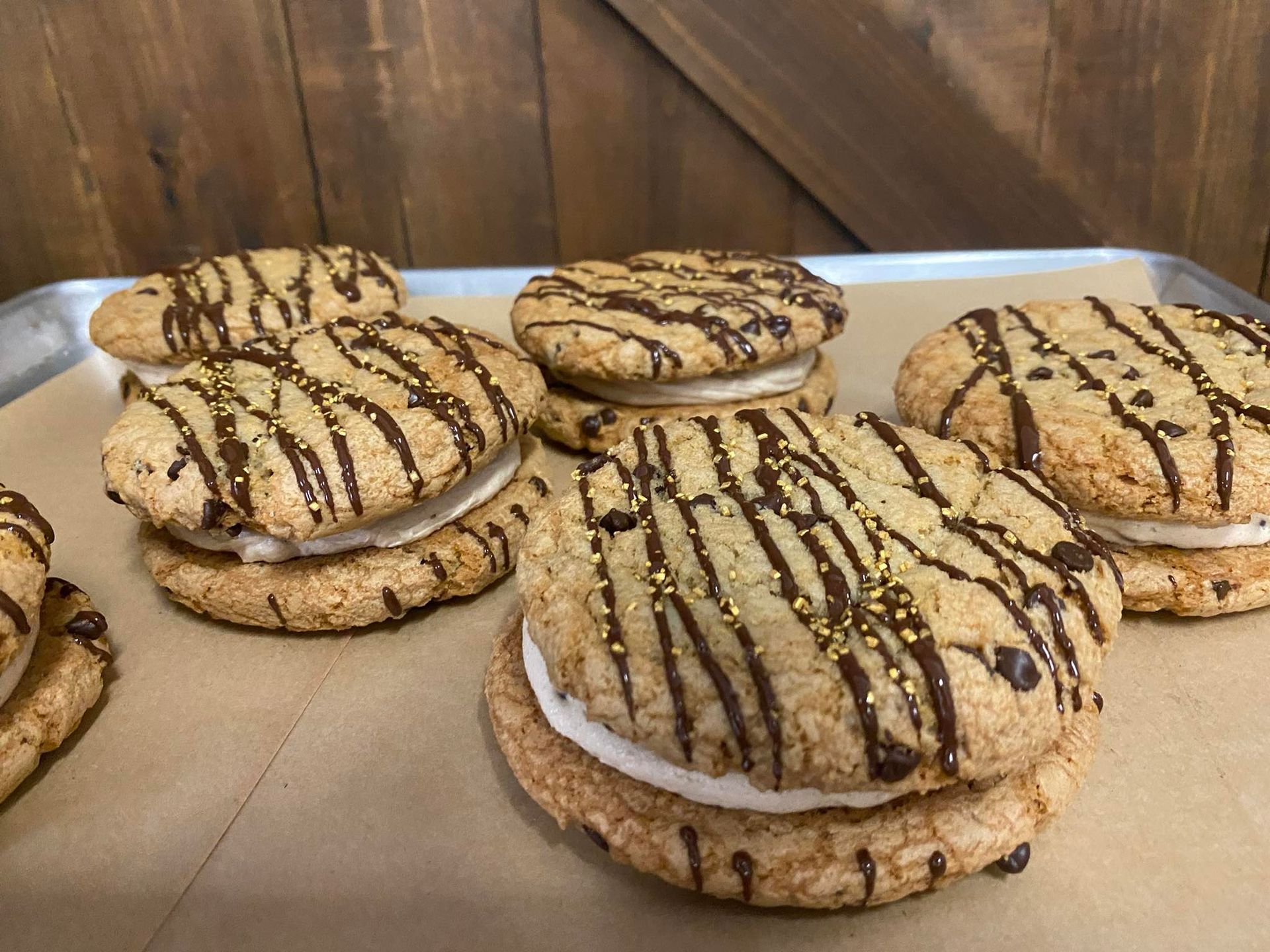Chocolate chip cookie sandwiches drizzled with chocolate, on a baking sheet.