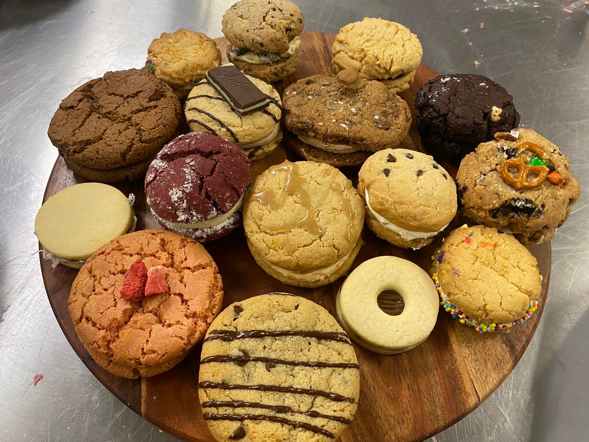 Assortment of colorful cookies, some sandwich style, arranged on a wooden serving board.