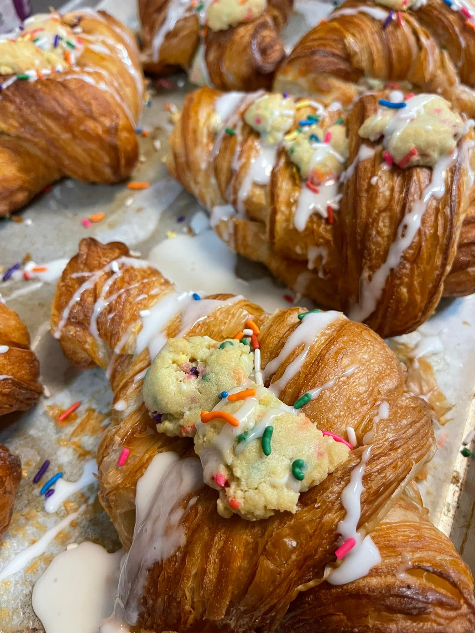 Croissant pastries with white icing, cookie dough, and sprinkles.