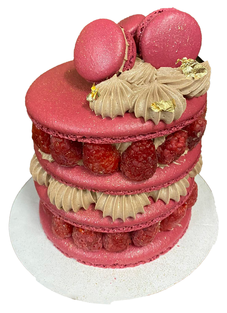 Pink macaron cake with layers of raspberries and chocolate frosting, topped with macarons and gold leaf.
