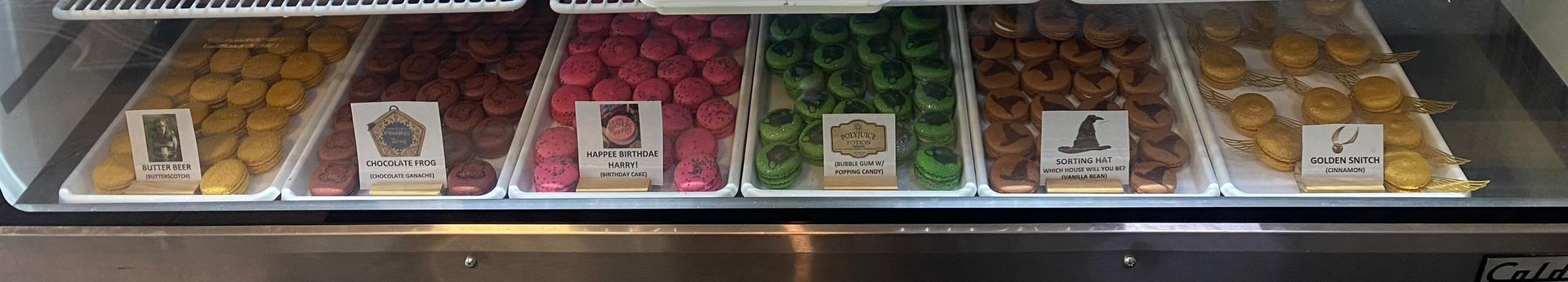 Display case of various colorful, round food items on white trays, each with a sign.