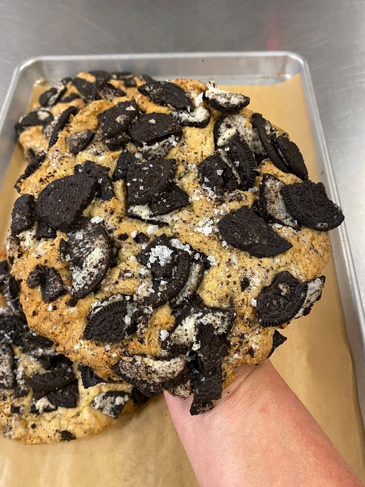 Large, round cookies with Oreo chunks on a tray, one held by a hand.