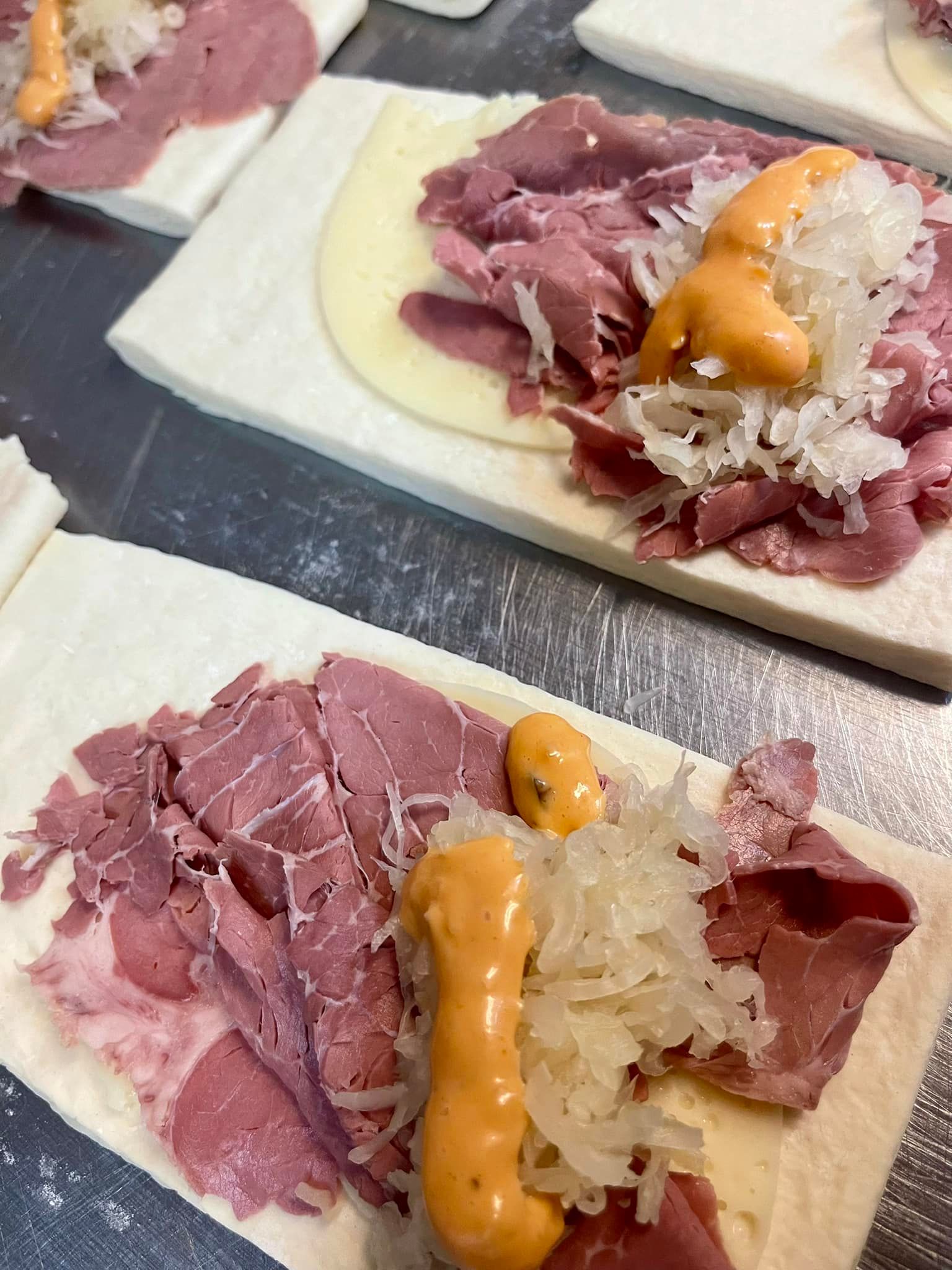 Close-up of prepared corned beef sandwiches with sauerkraut and sauce on white bread.
