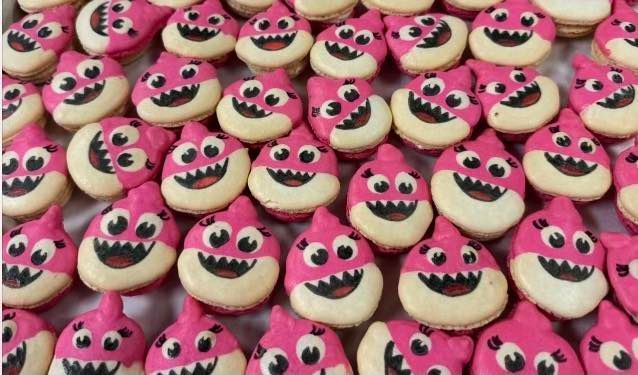 Rows of pink and cream-colored shark-shaped macarons with black eyes and smiles.