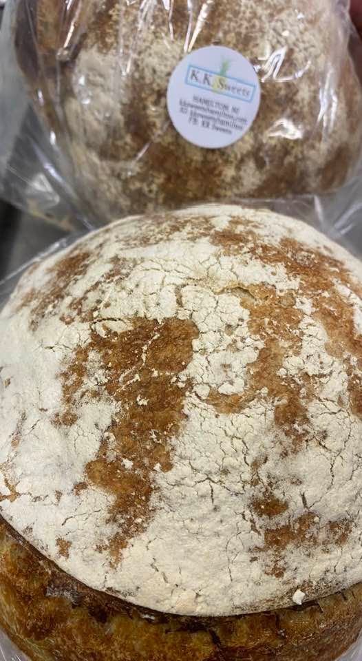 Two round loaves of bread, one in front, showing a crusty exterior dusted with flour. The top loaf is wrapped in plastic.