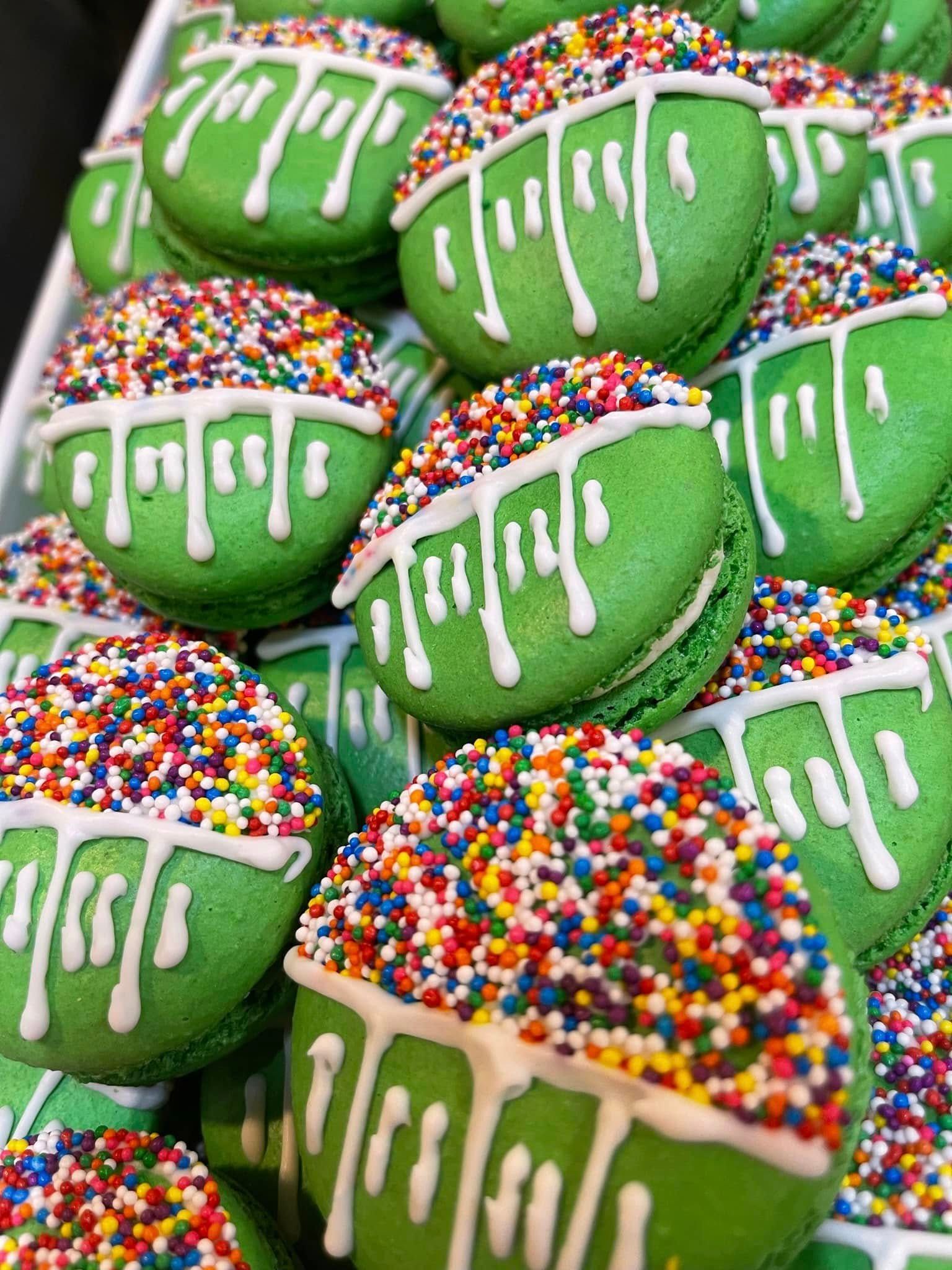 Green macarons with white drizzled icing and colorful sprinkles.