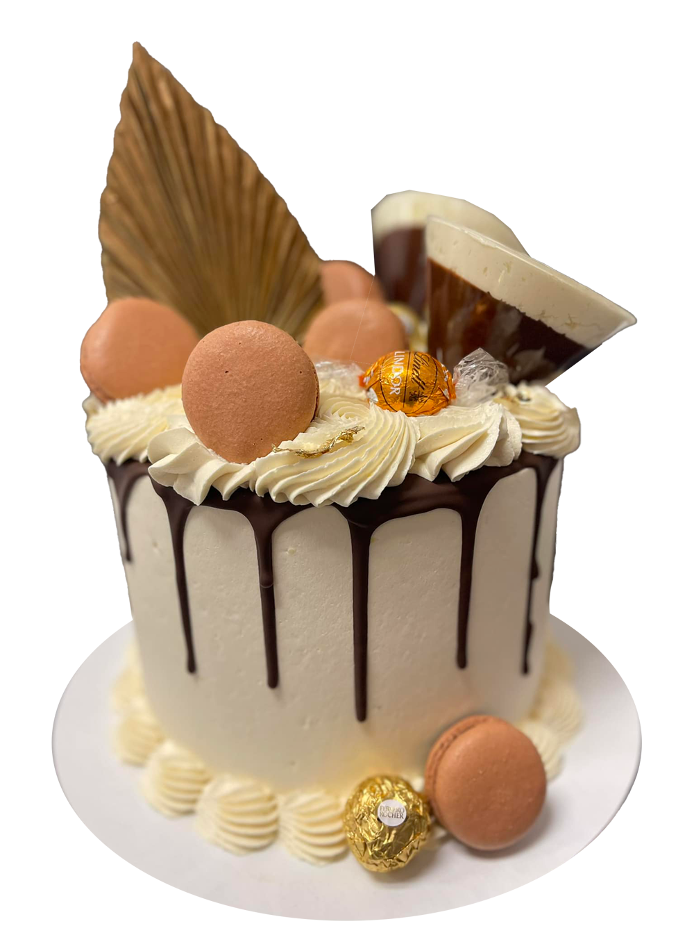 Cake with white frosting, chocolate drips, decorated with macarons, dried leaves, and chocolate.