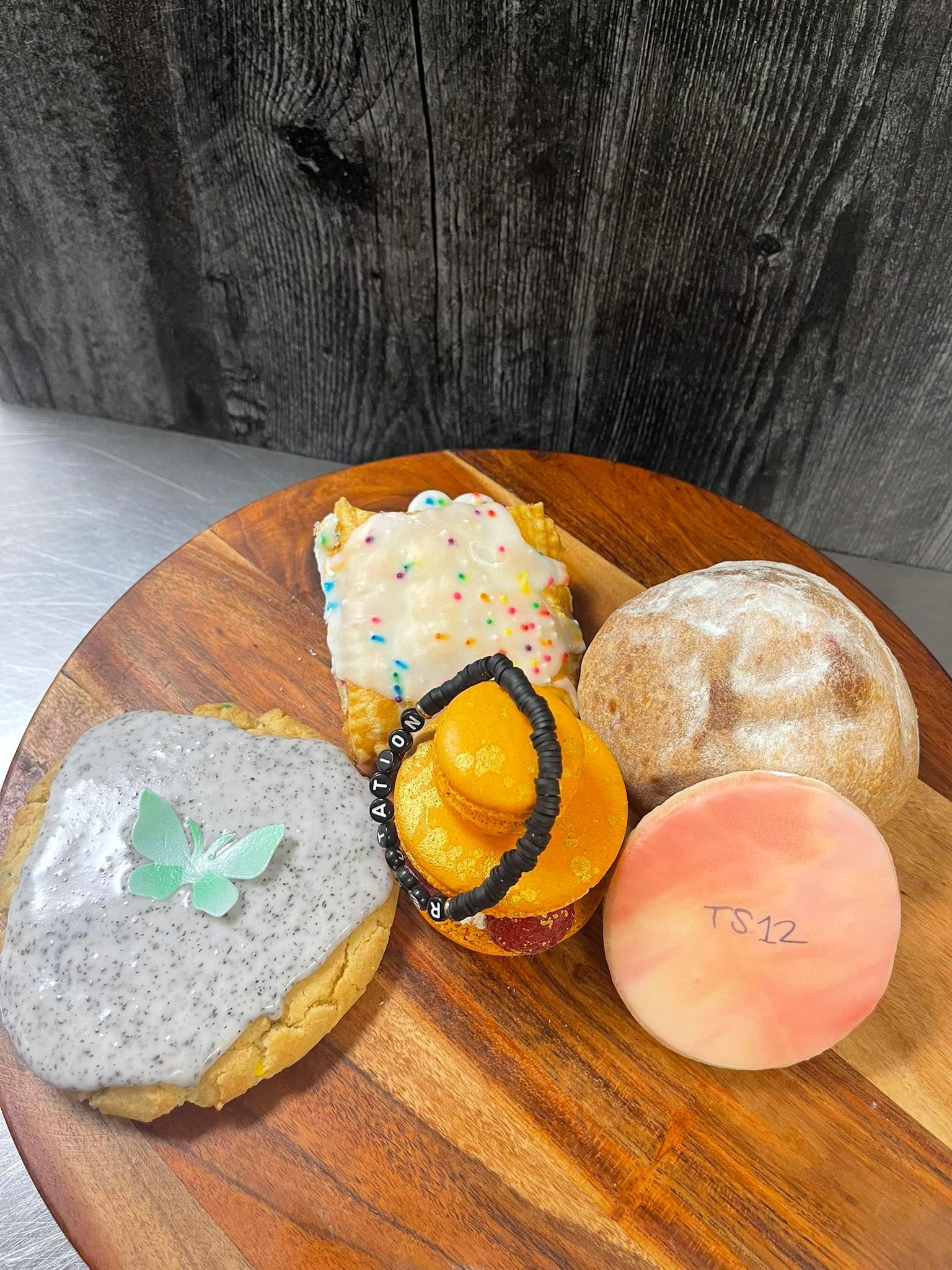 Assortment of decorated pastries on a wooden board: frosted cookies, donut, and cupcake, with colorful sprinkles.