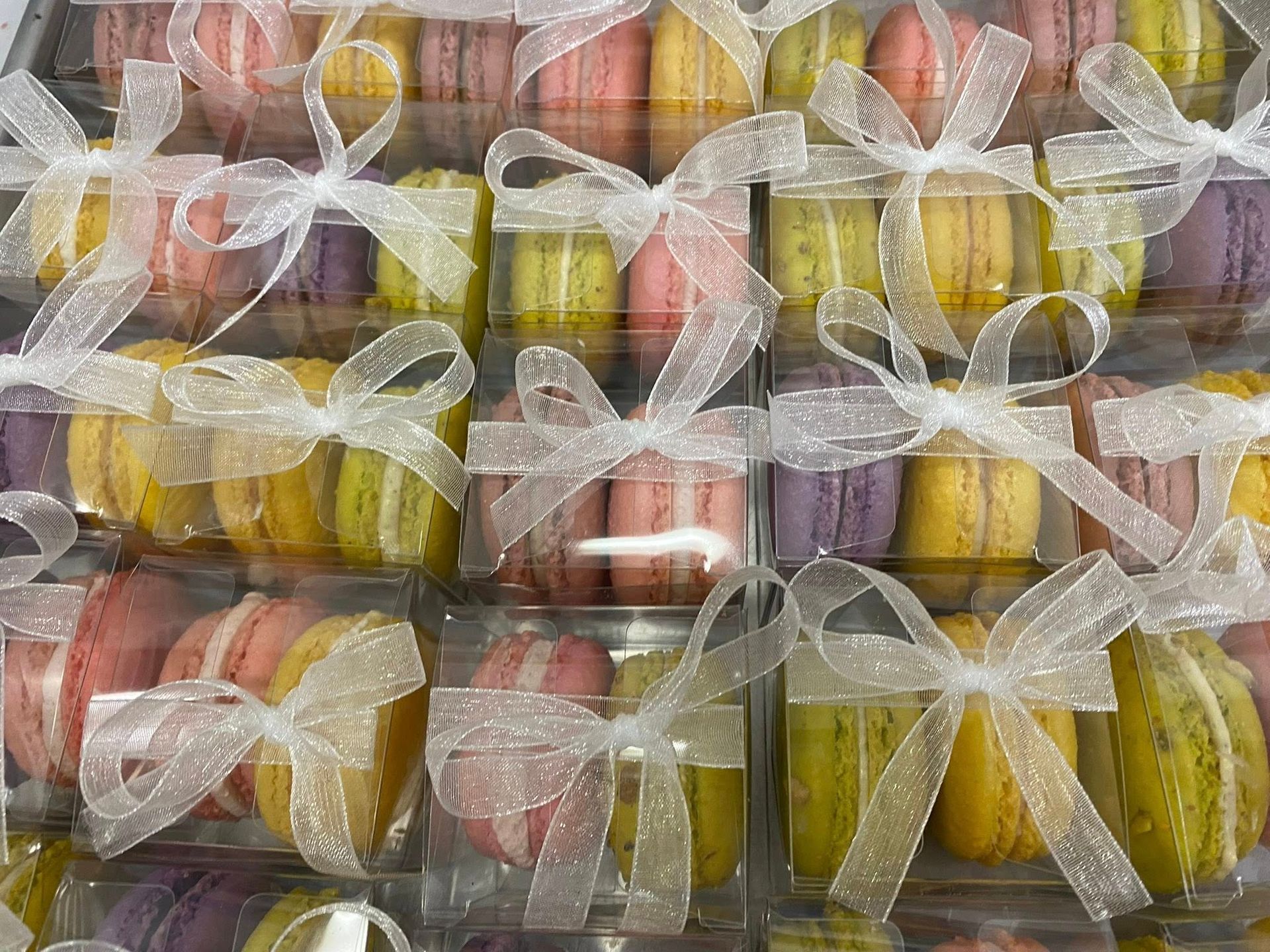 Colorful macarons in clear boxes tied with white ribbons.