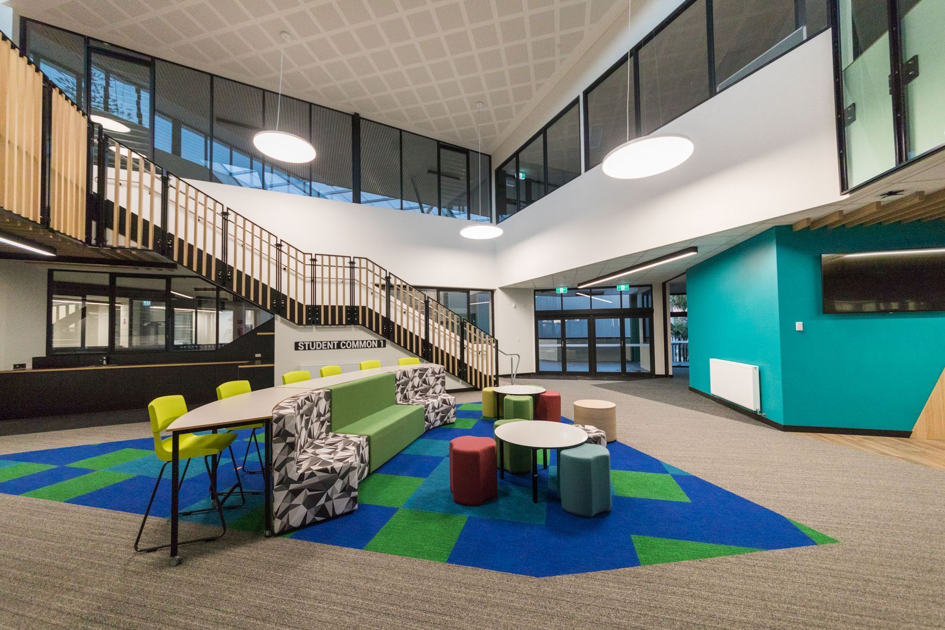 A modern school lobby with a prominent staircase, colorful modular seating, and geometric blue.