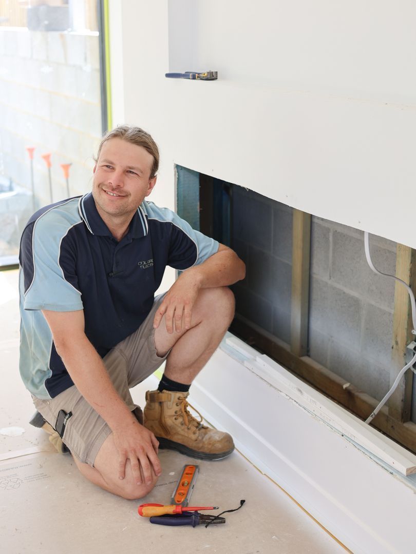 A professional kneels on a floor while installing wiring in a wall niche, with tools arranged nearby.