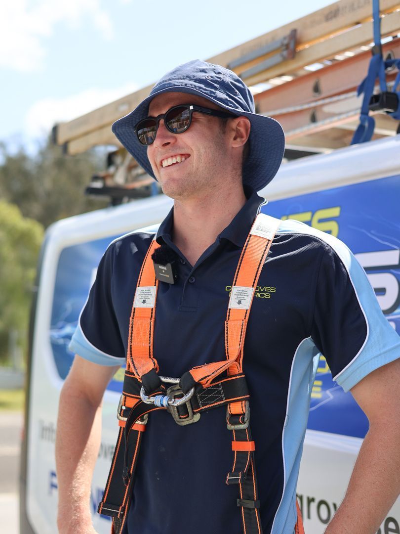 A person in a bucket hat, sunglasses, and safety harness stands in front of a work van.