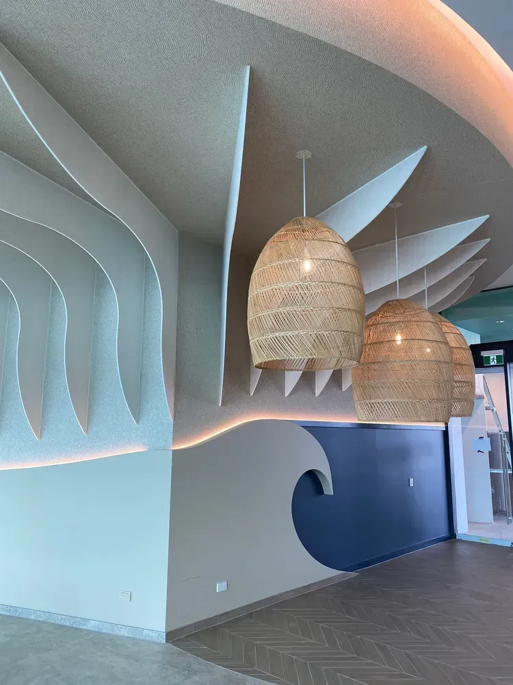 Interior view featuring textured, wave-like ceiling panels, rattan pendant lights, and a blue wall with a wave cutout.