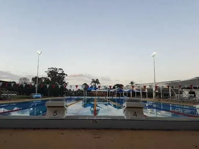 A wide-angle shot of an outdoor swimming pool with lane dividers, starting blocks labeled 4 and 5, under a clear sky.