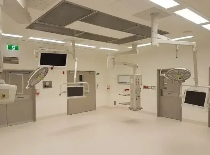 A bright, sterile hospital operating room featuring ceiling-mounted surgical lights, medical monitors, and equipment.