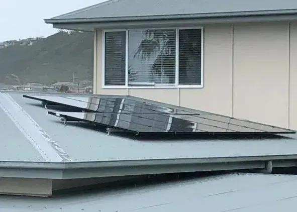 A set of black solar panels mounted on a gray, angled metal roof beneath a residential window.