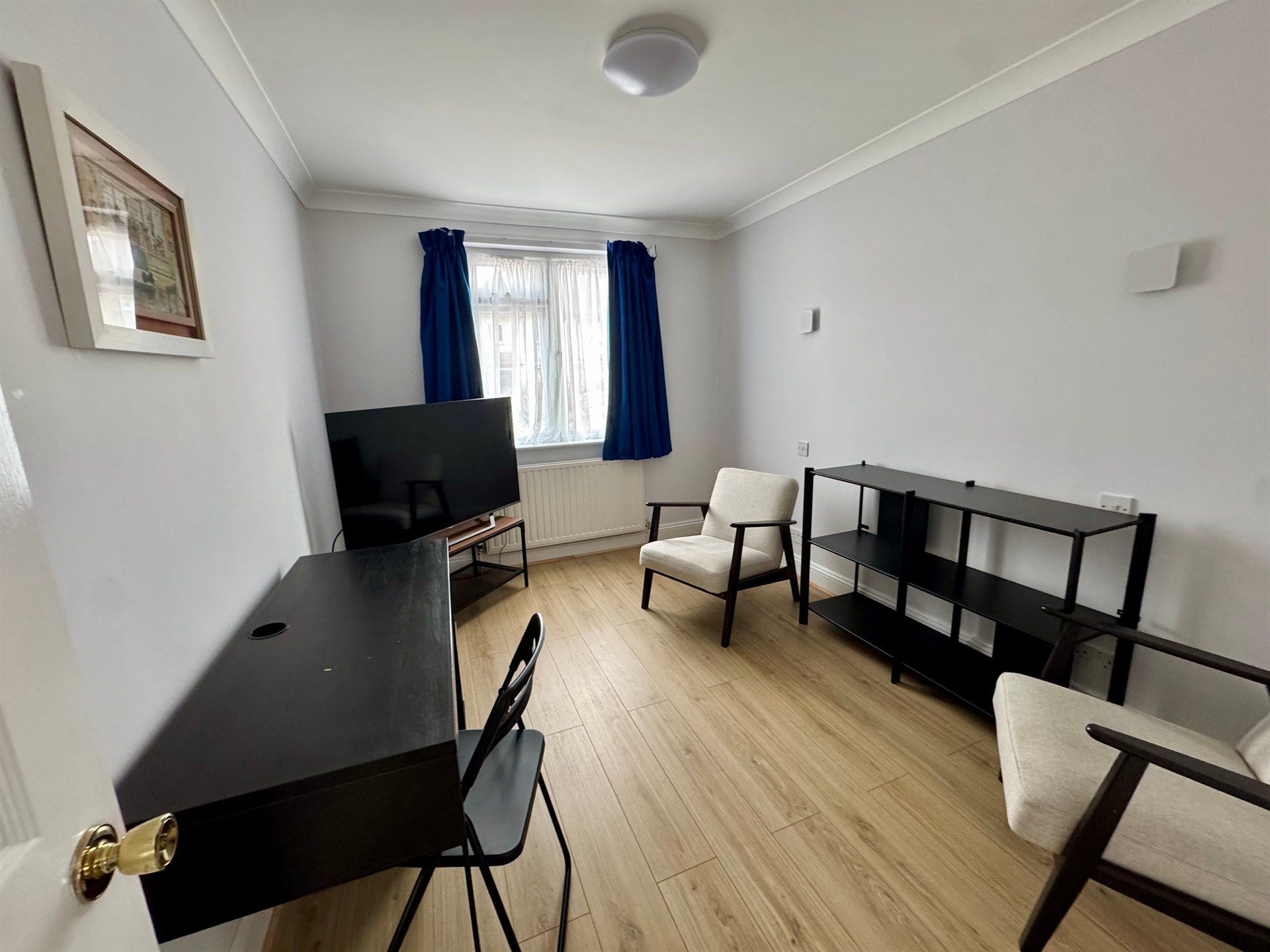 A living room with a desk , chairs , a television and a bookshelf.