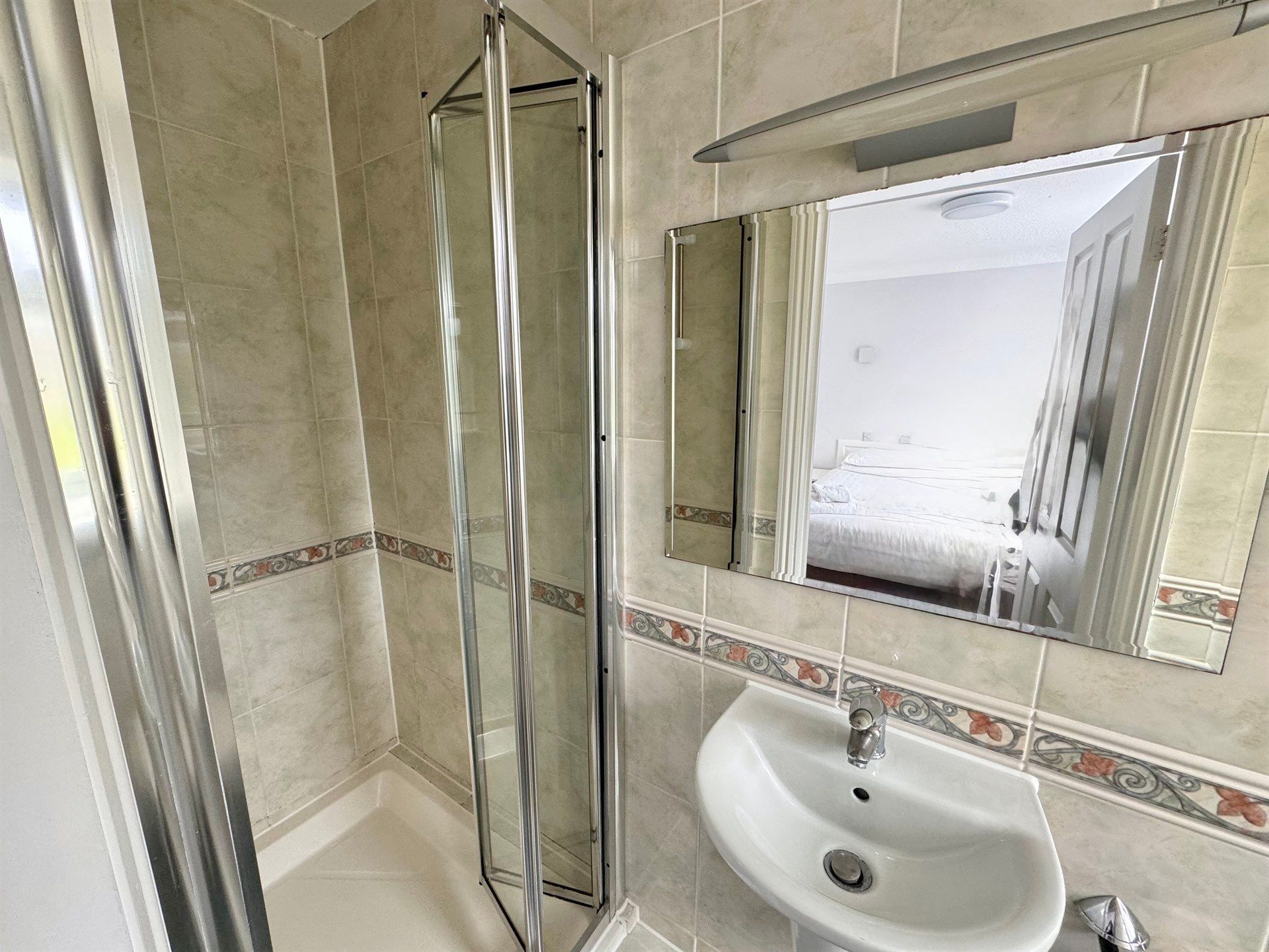 A bathroom with a sink , shower and mirror.