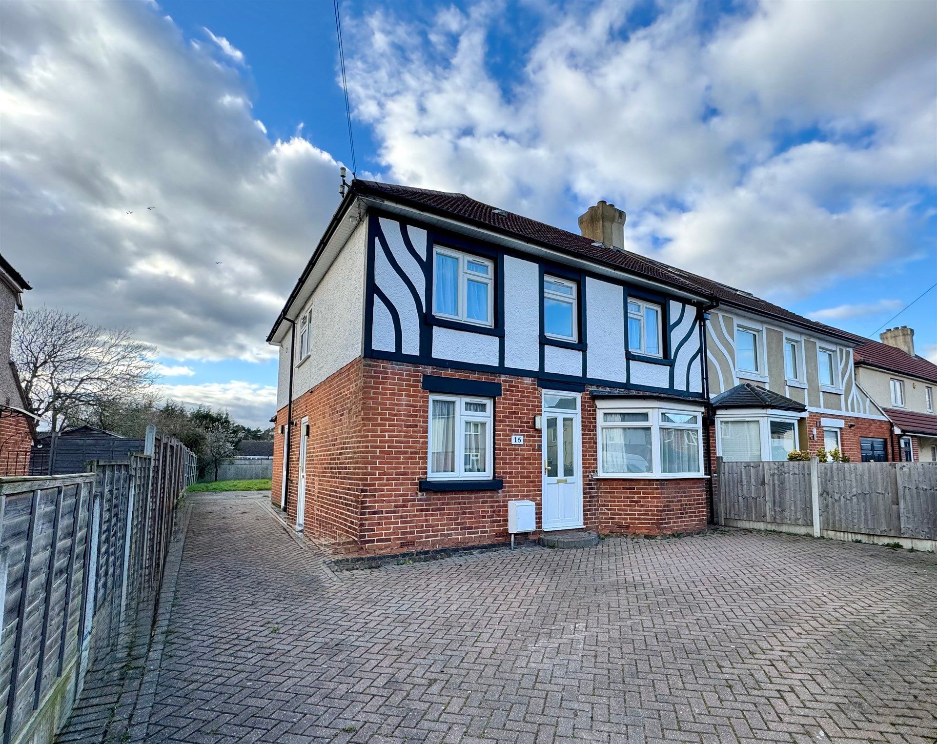 A brick house with a driveway and a fence in front of it.