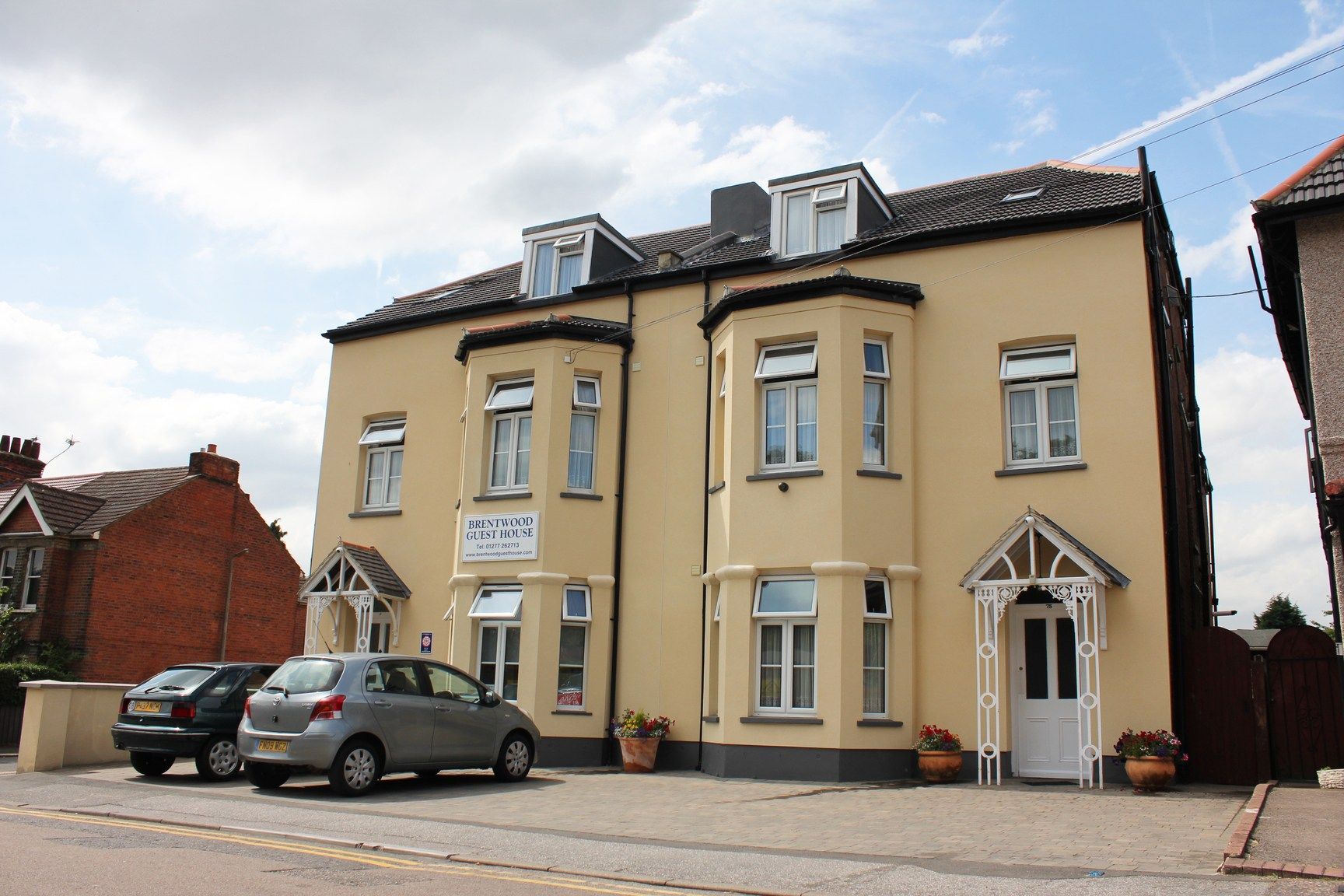 Two cars are parked in front of a large yellow building