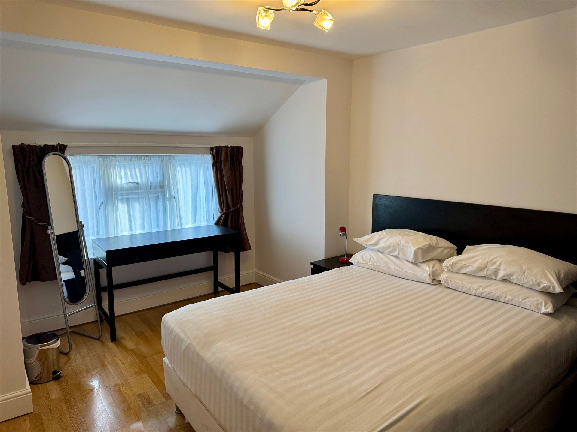 A bedroom with a bed , desk , mirror and window.