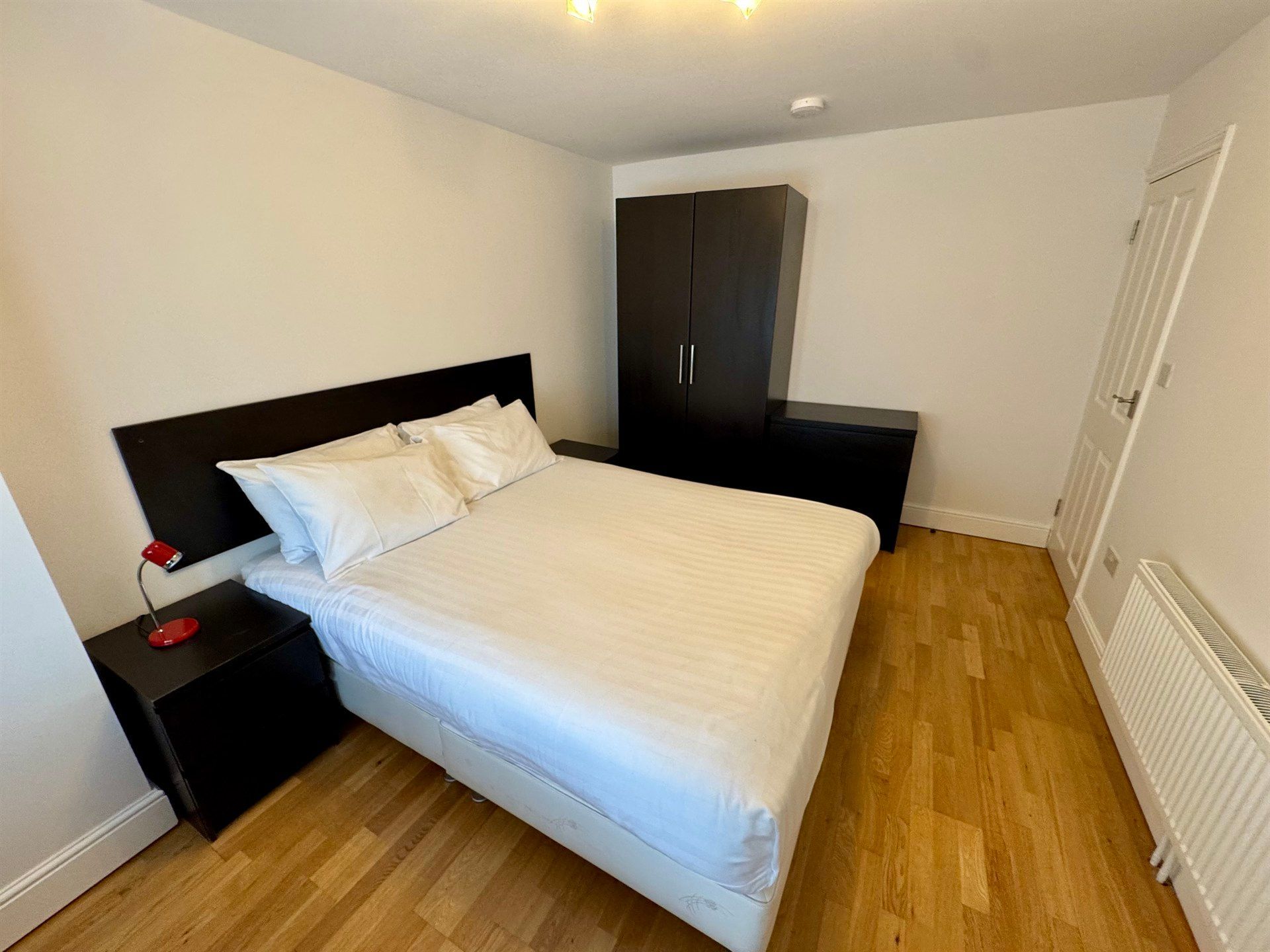 A bedroom with a bed , nightstand , and wardrobe.