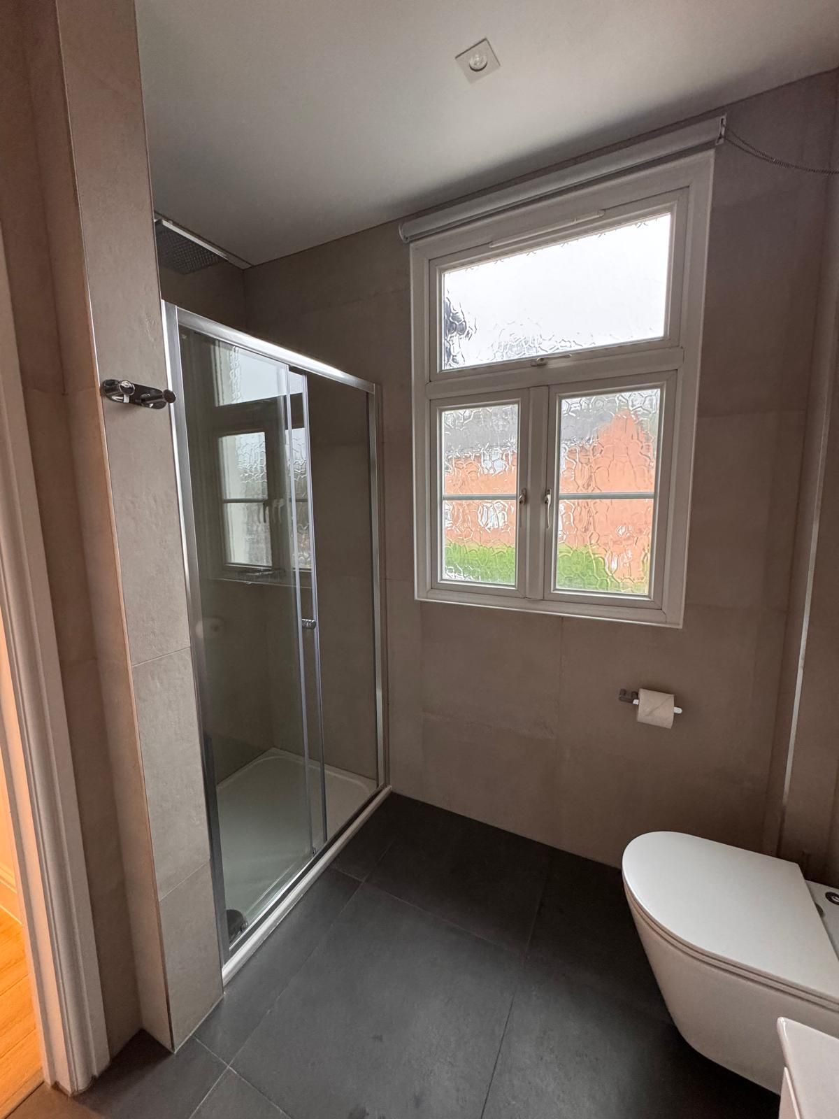 A bathroom with a toilet , shower and window.