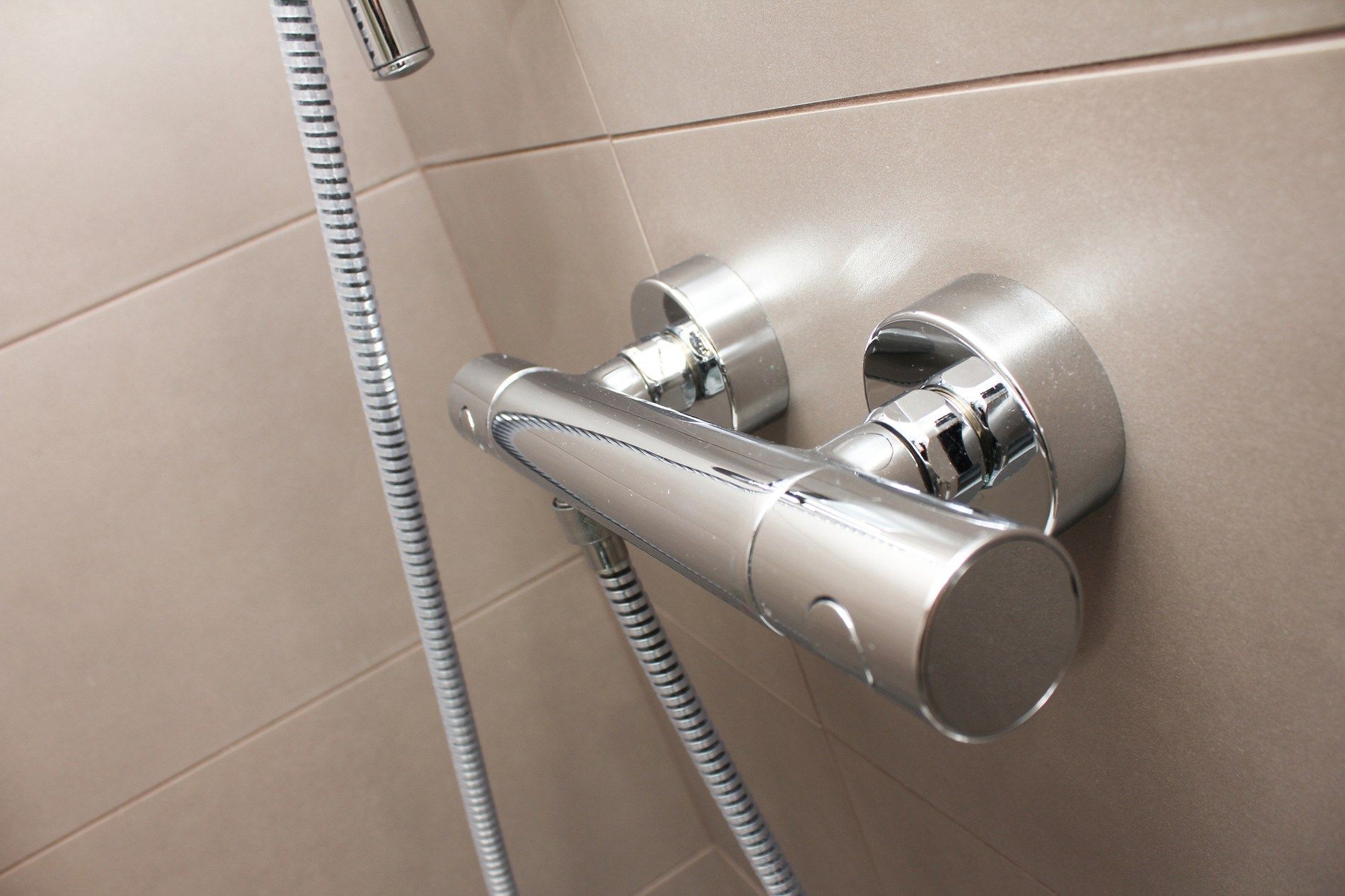 A close up of a shower faucet with a hose attached to it.