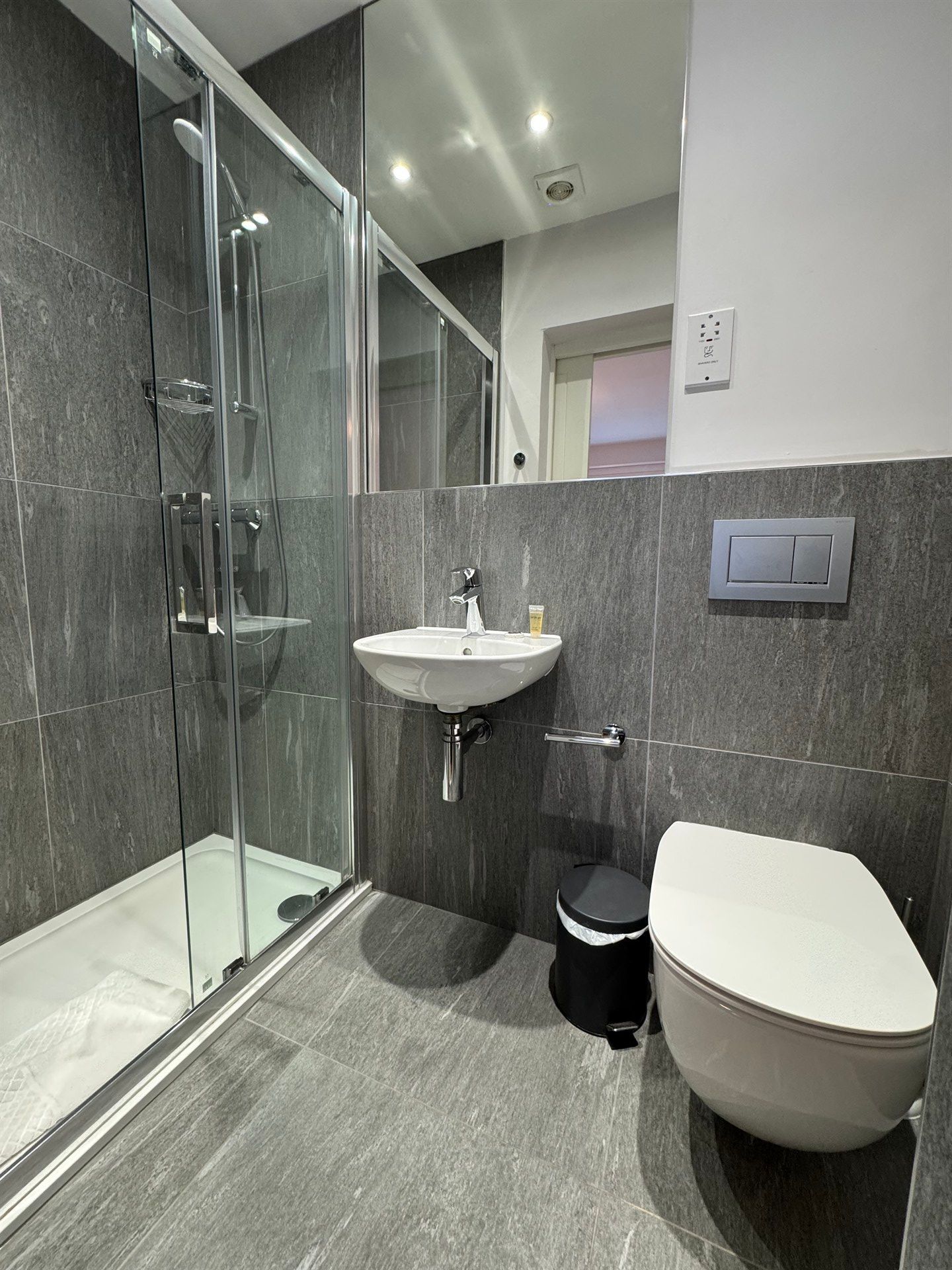 A bathroom with a toilet , sink , shower and mirror.