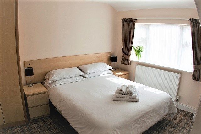 A bedroom with a bed , two nightstands , a window and a radiator.