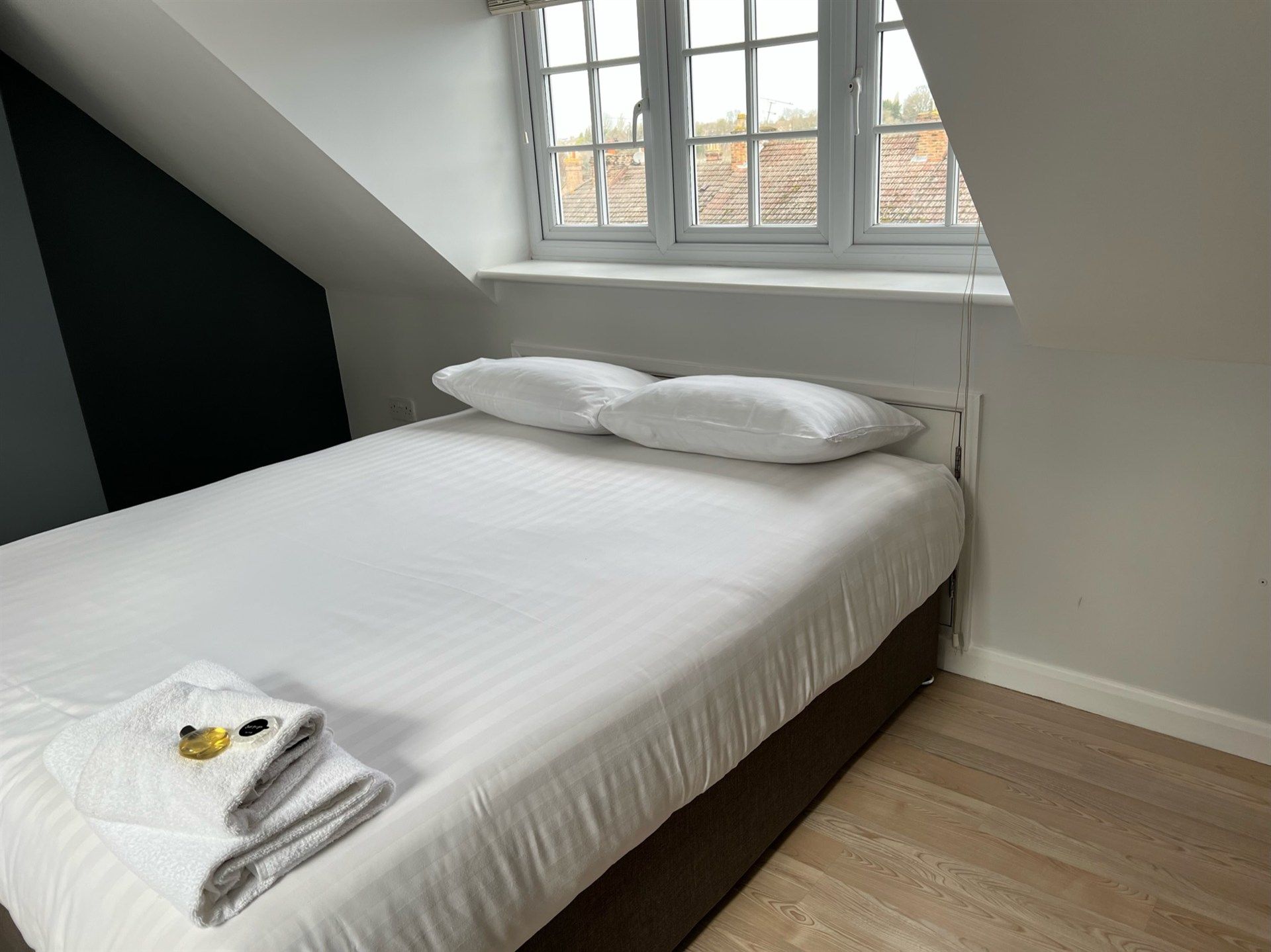 A bed with white sheets and pillows in a bedroom with a window.