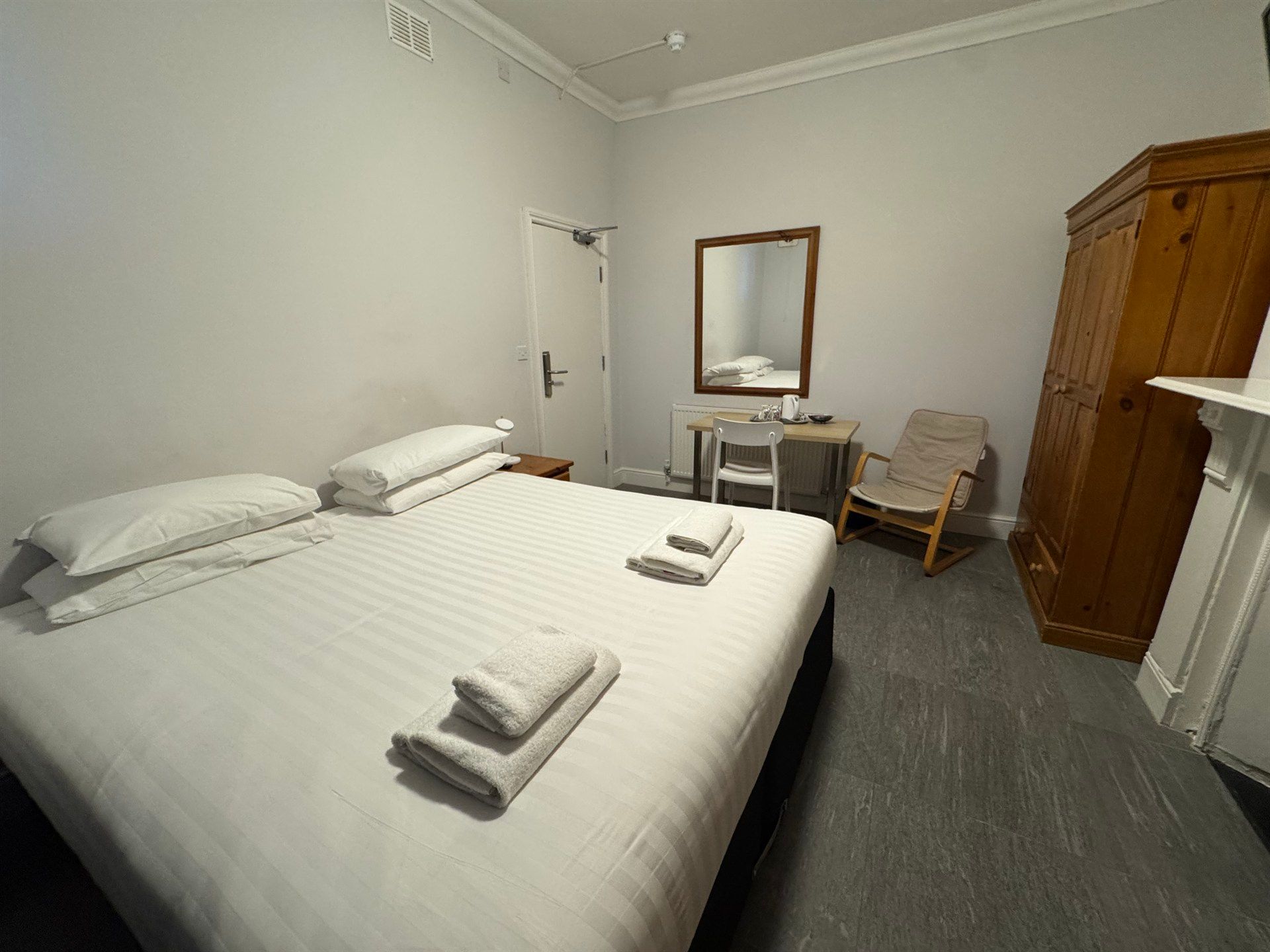 A hotel room with a bed , chair , desk and mirror.