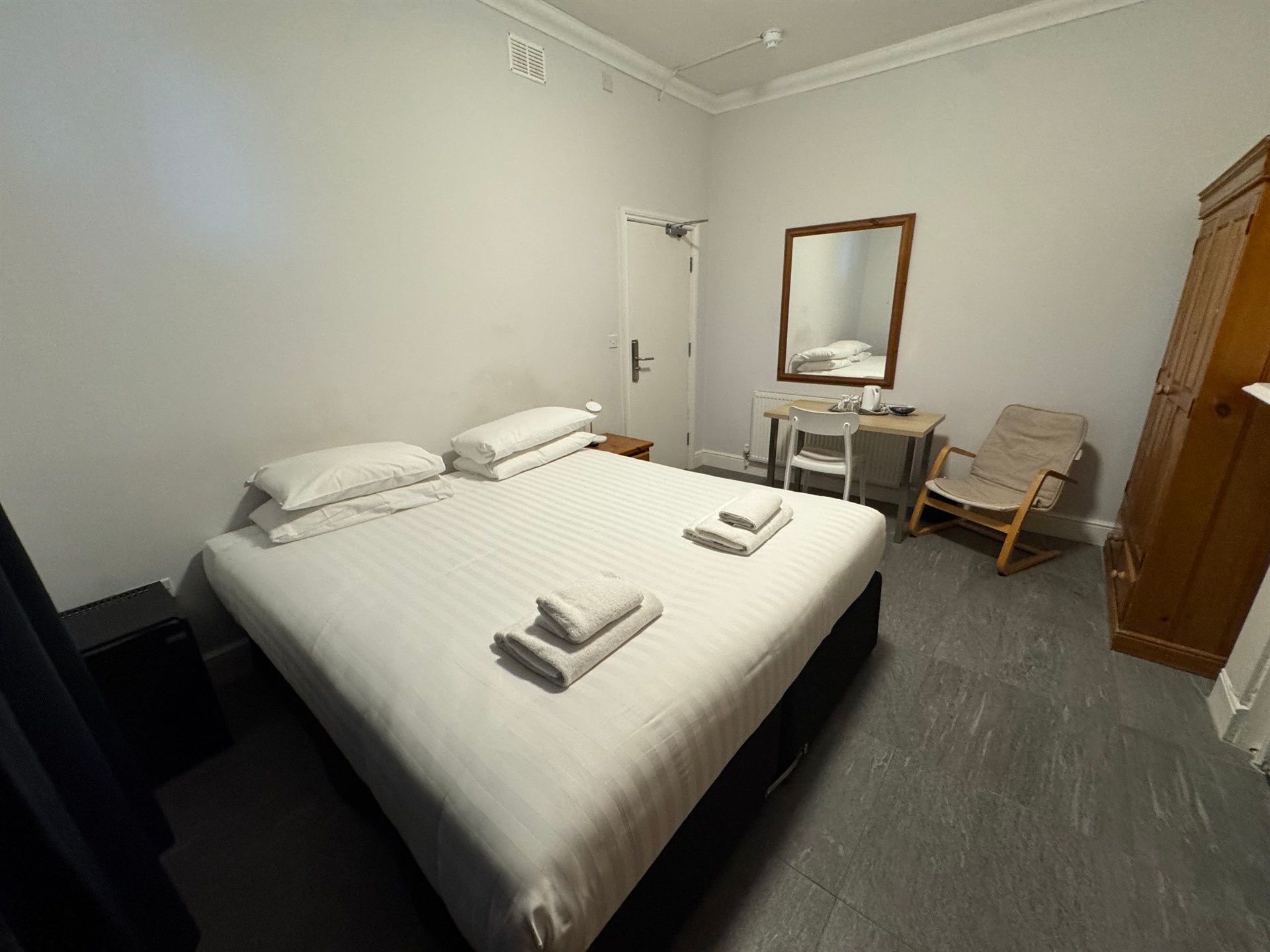 A hotel room with a bed , chair , desk and mirror.