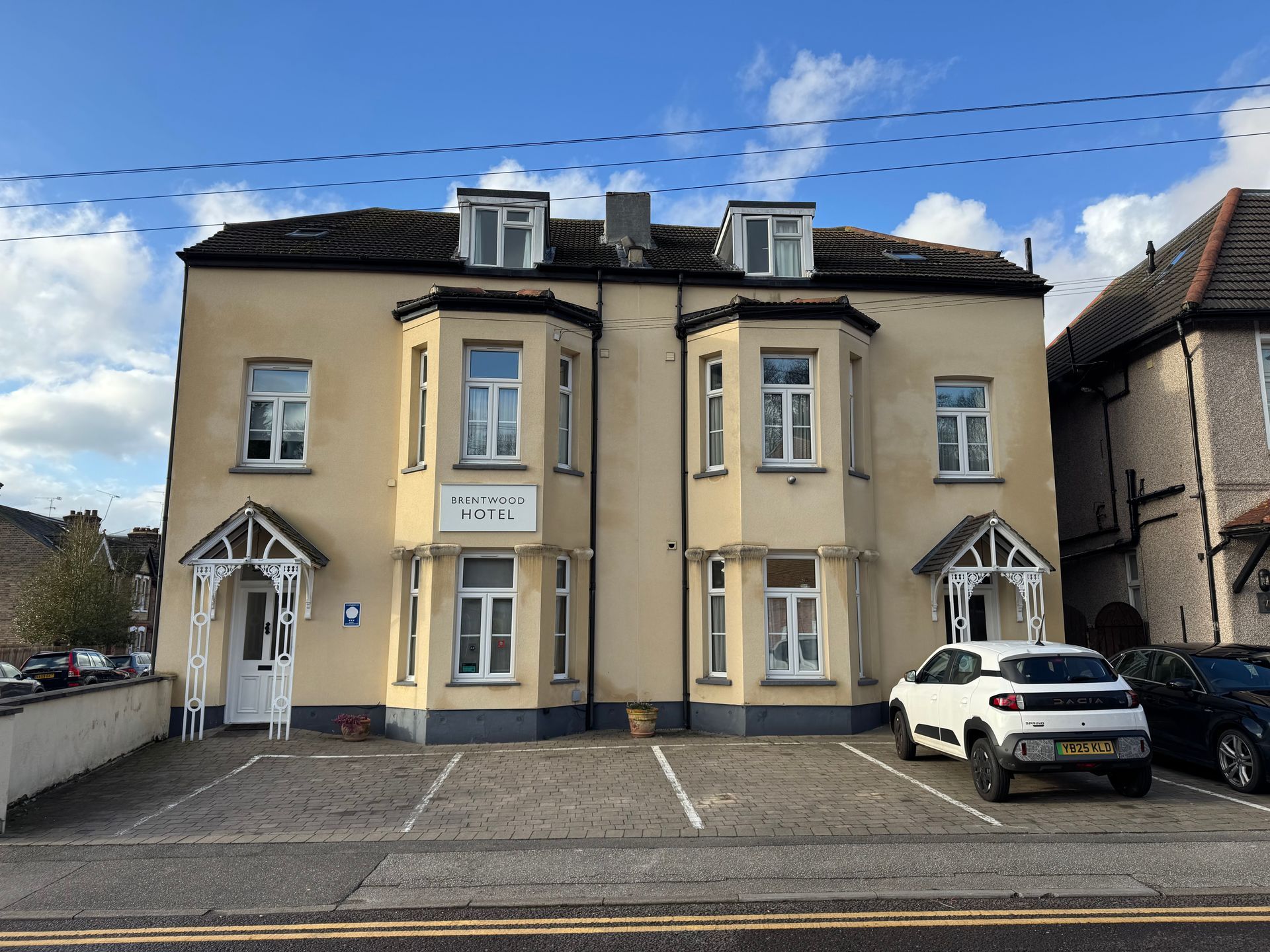 Yellow apartment building with parking spots; parked cars; blue sky.