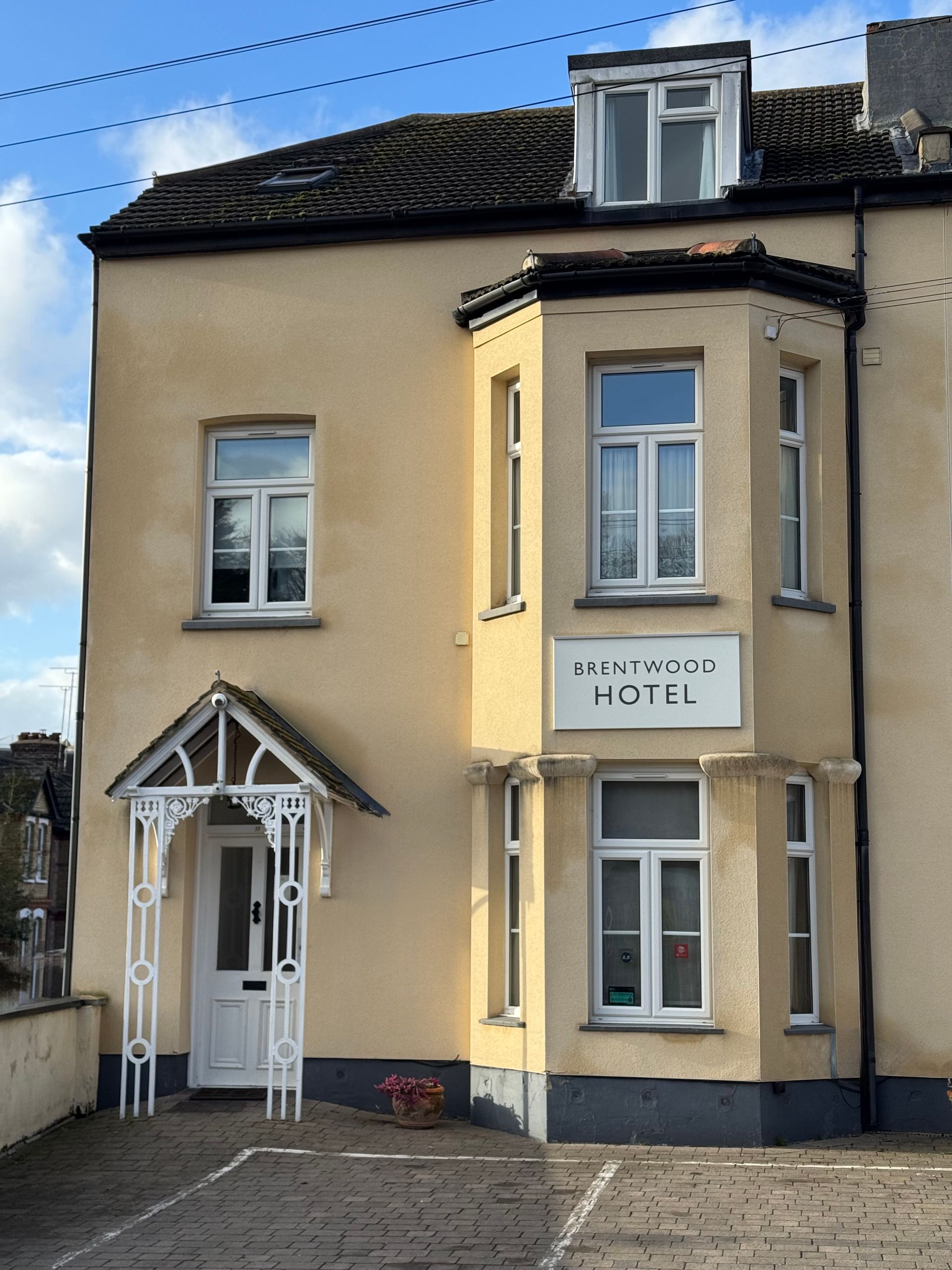Light yellow building with white trim, bay window, and small entry porch. 
