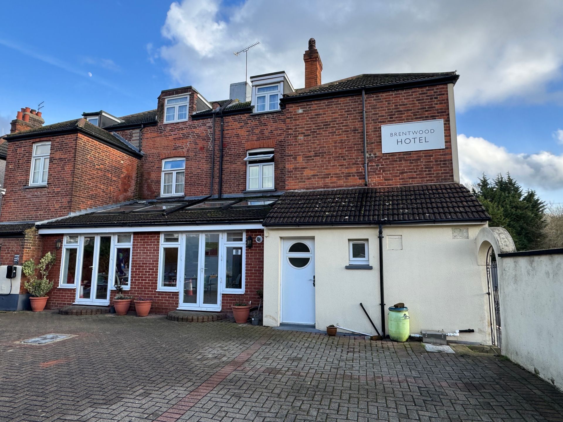 Brick building with windows and a white door, set on a brick paved area, under a blue sky.