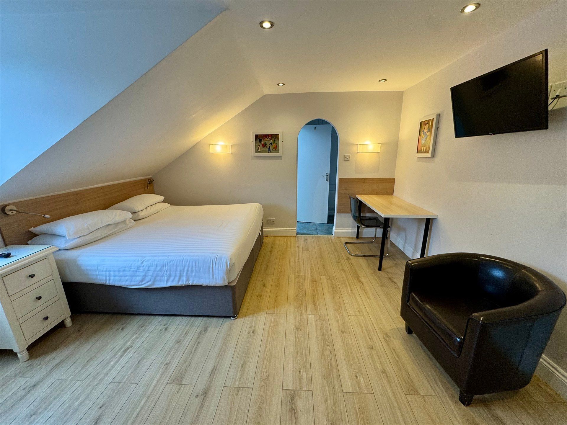 A hotel room with a bed , chair , desk and television.