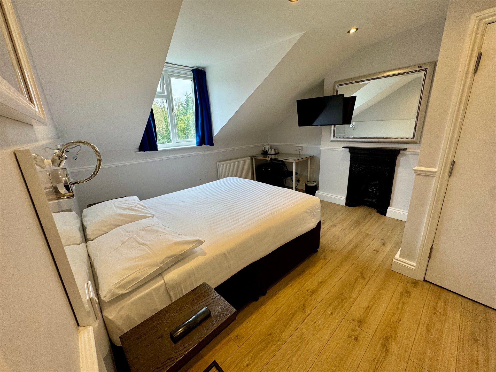 A bedroom with a bed , television , mirror and fireplace.