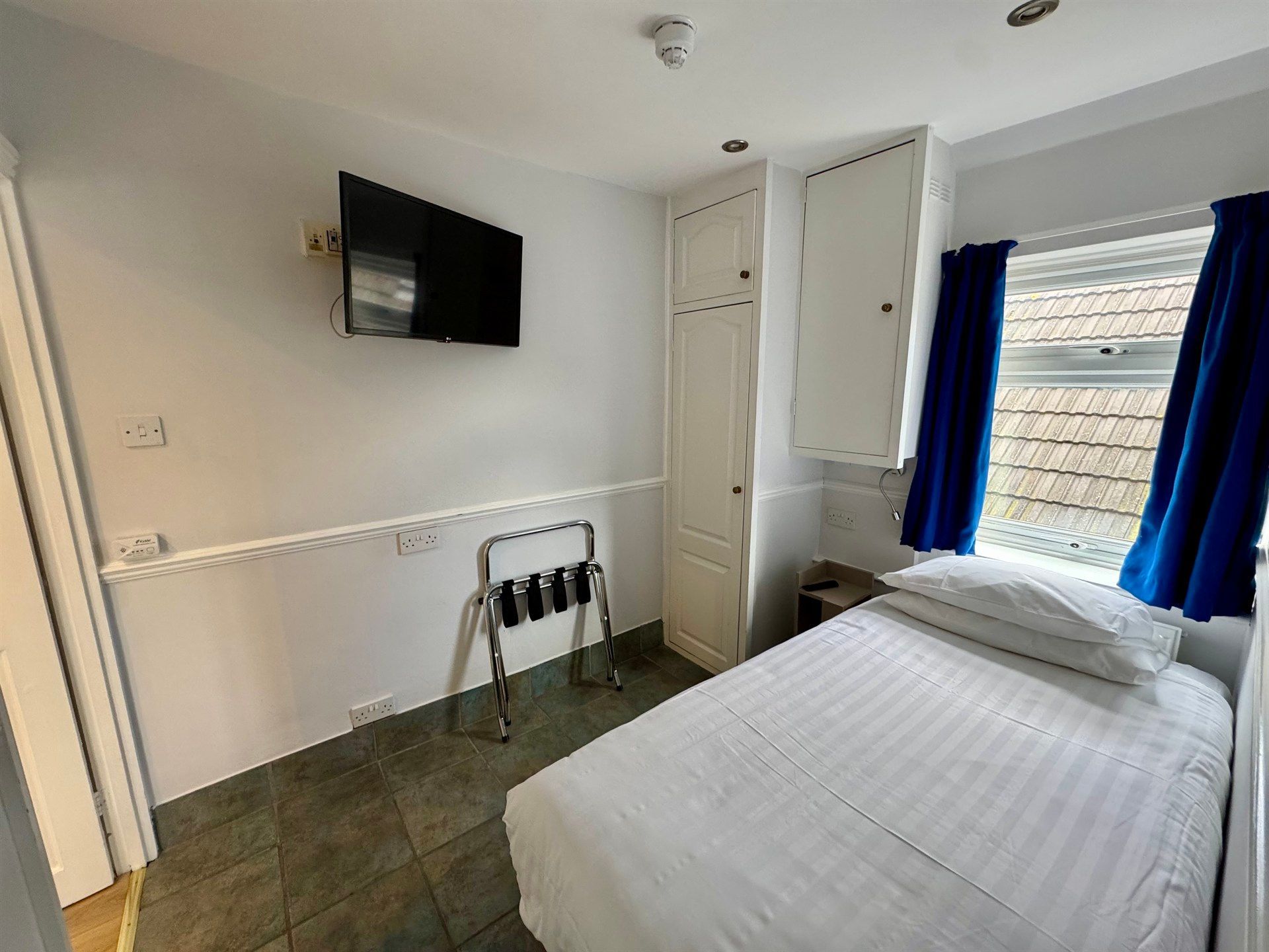 A hotel room with a single bed , television , and blue curtains.