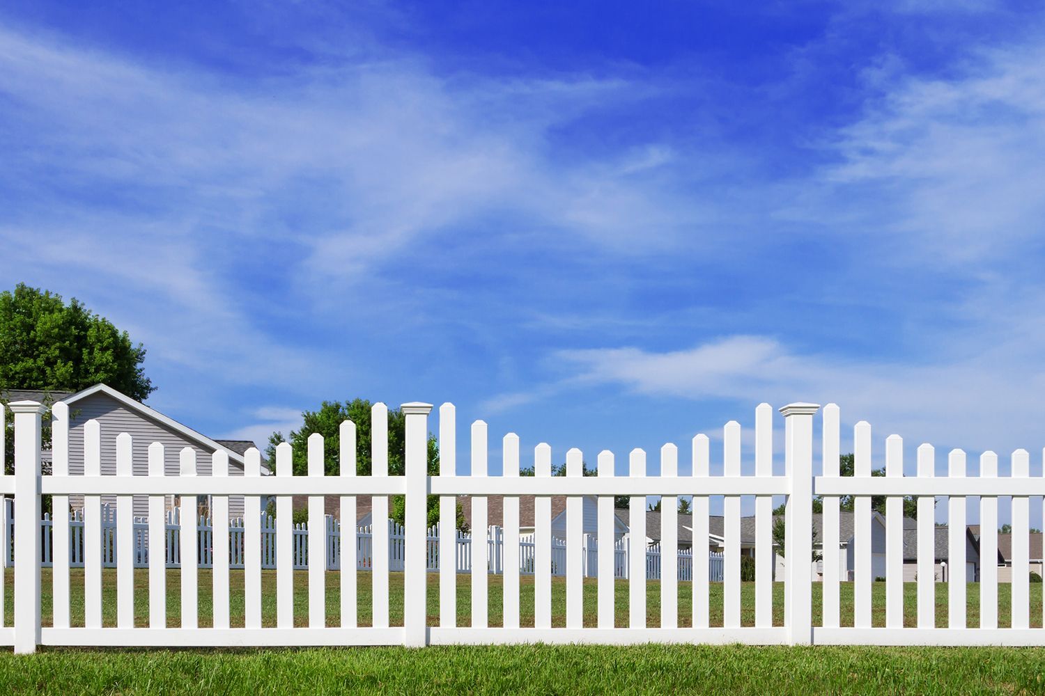 A white picket fence surrounds a grassy yard in front of a house.