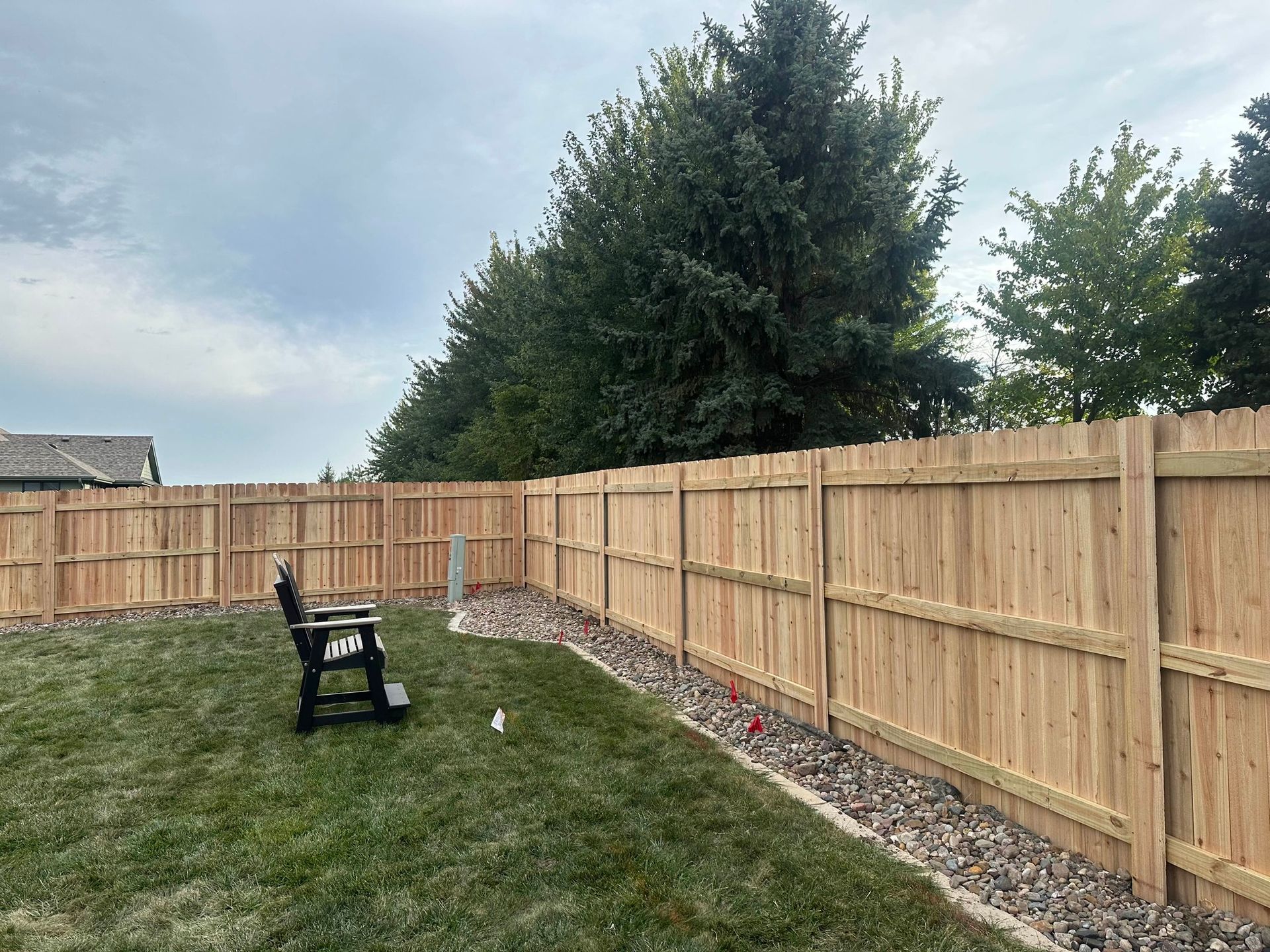 A wooden fence surrounds a lush green yard with a bench in the middle.