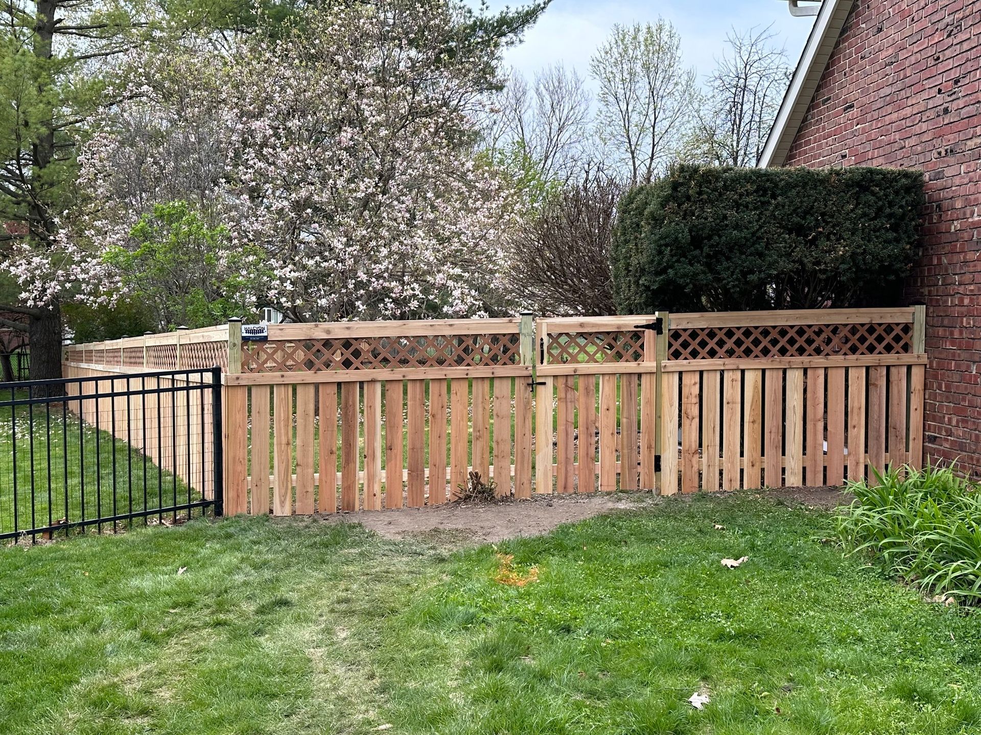 A wooden fence with a metal gate in front of a brick house.