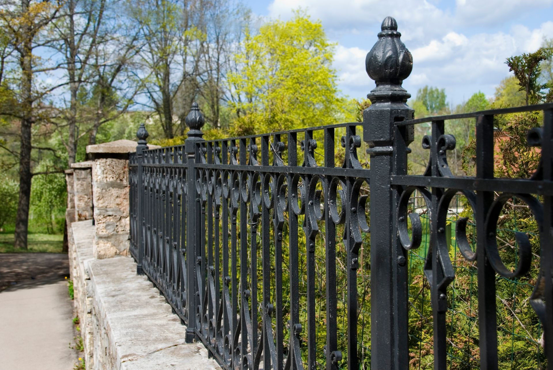 A black wrought iron fence surrounds a lush green hedge.