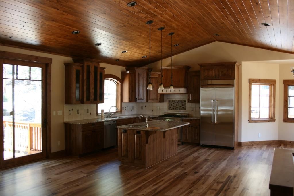 An empty kitchen with a wooden ceiling and hardwood floors