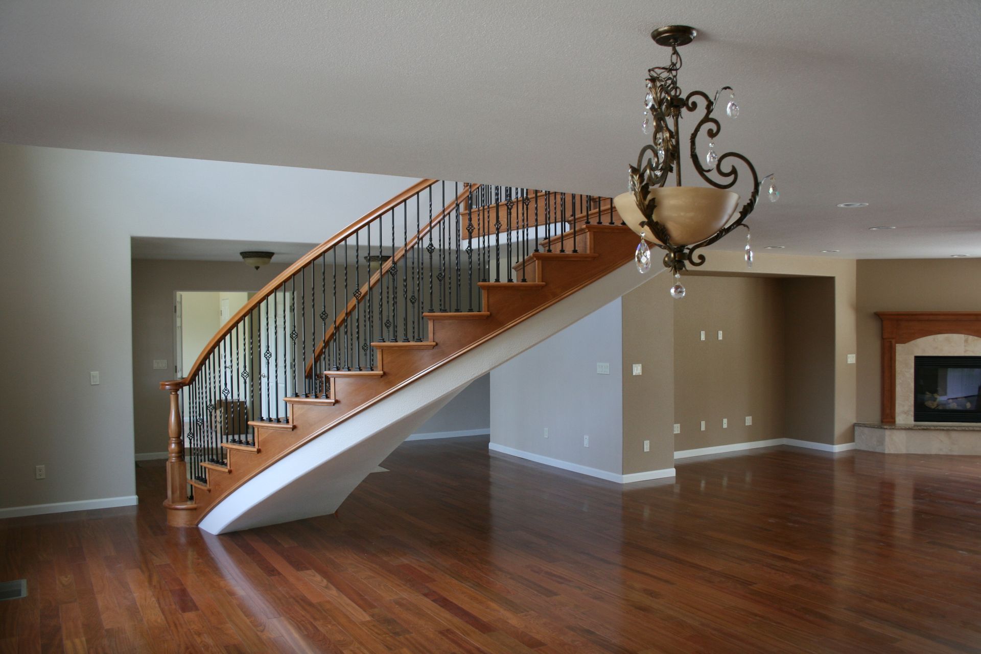 An empty living room with a curved staircase and a chandelier