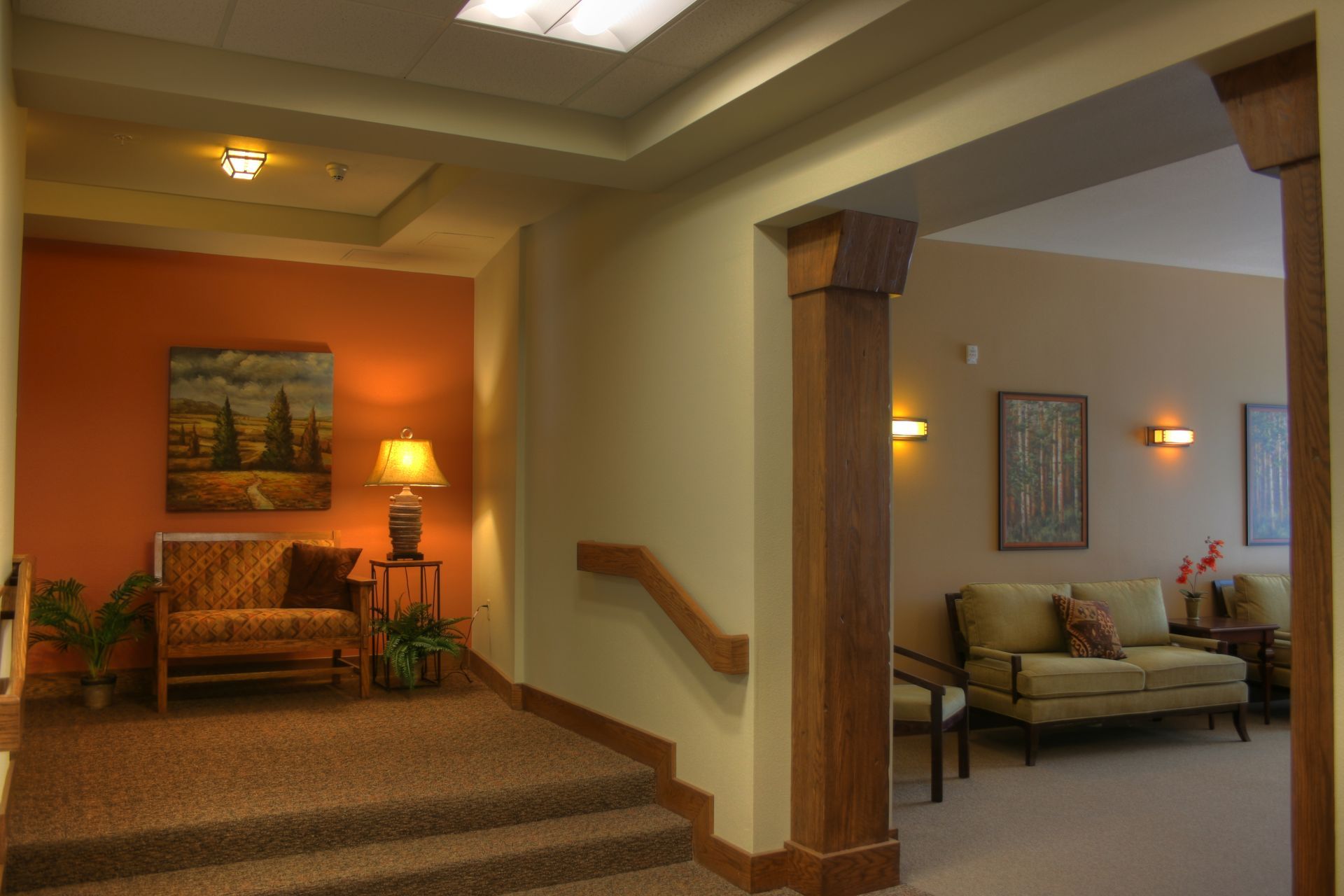 A hallway with stairs leading up to a living room with a couch and chairs.