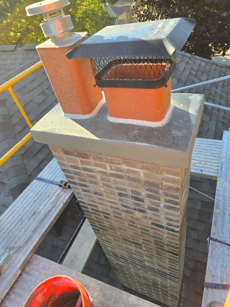 Brick chimney with two orange flues and a chimney cap on a rooftop.
